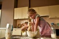 Cute little girl in apron kneading dough while making cookies together with her brother on the kitchen table at home Royalty Free Stock Photo