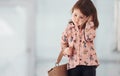 Cute little girl with bag indoors in the office or airport talking by phone Royalty Free Stock Photo