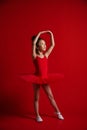 Cute little girl ballerina dancer in beautiful dress is dancing jumping on red background Royalty Free Stock Photo