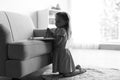 Cute little girl with beads praying over Bible in living room, black and white effect. Royalty Free Stock Photo