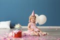 Cute little girl in birthday party cap with gift box sitting on furry rug indoors Royalty Free Stock Photo