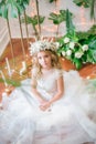 Cute little girl with blond curly hair in a white wedding dress and a wreath of flowers in floral decorations Royalty Free Stock Photo