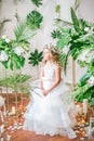 Cute little girl with blond curly hair in a white wedding dress and a wreath of flowers in floral decorations Royalty Free Stock Photo