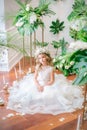 Cute little girl with blond curly hair in a white wedding dress and a wreath of flowers in floral decorations Royalty Free Stock Photo