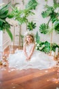 Cute little girl with blond curly hair in a white wedding dress and a wreath of flowers in floral decorations Royalty Free Stock Photo