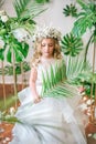 Cute little girl with blond curly hair in a white wedding dress and a wreath of flowers in floral decorations Royalty Free Stock Photo