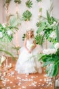 Cute little girl with blond curly hair in a white wedding dress and a wreath of flowers in floral decorations Royalty Free Stock Photo