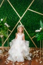 Cute little girl with blond curly hair in a white wedding dress and a wreath of flowers in floral decorations Royalty Free Stock Photo