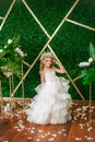 Cute little girl with blond curly hair in a white wedding dress and a wreath of flowers in floral decorations Royalty Free Stock Photo