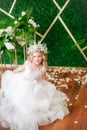 Cute little girl with blond curly hair in a white wedding dress and a wreath of flowers in floral decorations Royalty Free Stock Photo