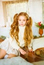 Cute little girl with blond long curly hair in a light knitted sweater by the festive fireplace with garlands Royalty Free Stock Photo