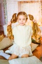 Cute little girl with blond long curly hair in a light knitted sweater by the festive fireplace with garlands Royalty Free Stock Photo