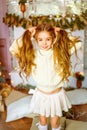 Cute little girl with blond long curly hair in a light knitted sweater by the festive fireplace with garlands Royalty Free Stock Photo