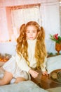 Cute little girl with blond long curly hair in a light knitted sweater by the festive fireplace with garlands Royalty Free Stock Photo