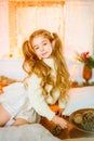 Cute little girl with blond long curly hair in a light knitted sweater by the festive fireplace with garlands Royalty Free Stock Photo