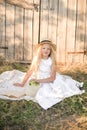 Cute little girl with blond long hair in a summer field at sunset with a white dress with a straw hat Royalty Free Stock Photo