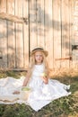 Cute little girl with blond long hair in a summer field at sunset with a white dress with a straw hat Royalty Free Stock Photo