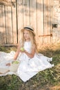 Cute little girl with blond long hair in a summer field at sunset with a white dress with a straw hat Royalty Free Stock Photo