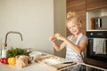 Little girl standing at crop mother and cracking egg to flour on kitchen. Royalty Free Stock Photo