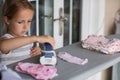 Cute little girl with blonde hair is leaning on ironing clothes on board at home. Daughter helping to mother ironing clothes for Royalty Free Stock Photo