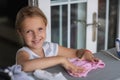 Cute little girl with blonde hair is leaning on ironing clothes on board at home. Daughter helping to mother ironing clothes for Royalty Free Stock Photo