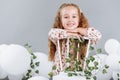 Cute little girl blonde smiling having fun in studio with white balloons and green. child in floral dress sitting on white chair Royalty Free Stock Photo