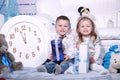 Cute little girl and boy with gifts boxes and big white clock sitting near the white sofa in Christmas and New Year studio Royalty Free Stock Photo