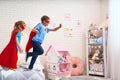 Cute little girl and boy jumping from bed to fly, play superhero with cloak and mask at home in kids bedroom Royalty Free Stock Photo