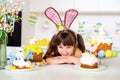 Cute little girl with bunny ears in the kitchen is smiling near the Easter cake Royalty Free Stock Photo
