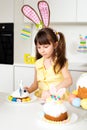 A cute little girl with bunny ears prepares an Easter cake and painted eggs. Religious holiday Royalty Free Stock Photo