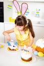 A cute little girl with bunny ears prepares an Easter cake and painted eggs. Religious holiday Royalty Free Stock Photo