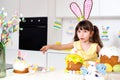 A cute little girl with bunny ears prepares an Easter cake and painted eggs. Religious holiday Royalty Free Stock Photo