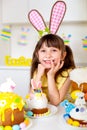 A cute little girl with bunny ears prepares an Easter cake and painted eggs. Religious holiday Royalty Free Stock Photo