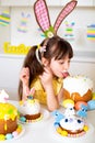 A cute little girl with bunny ears prepares an Easter cake and painted eggs. Religious holiday Royalty Free Stock Photo