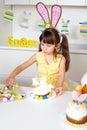 A cute little girl with bunny ears shows how beautiful it is to decorate an Easter cake Royalty Free Stock Photo