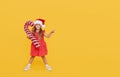 A cute little girl child in a fancy dress and a Santa hat holds an inflatable shape of a candy cane on a yellow background. 2021 Royalty Free Stock Photo