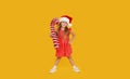 A cute little girl child in a fancy dress and a Santa hat holds an inflatable shape of a candy cane on a yellow background. 2021 Royalty Free Stock Photo