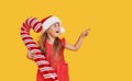 A cute little girl child in a fancy dress and a Santa hat holds an inflatable shape of a candy cane on a yellow background. 2021 Royalty Free Stock Photo