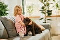 Cute little girl, child sitting on couch and playing with purebred dog, brown labrador at home. Happiness Royalty Free Stock Photo