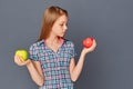 A cute little girl chooses between a green and red Apple on a gray background. The concept of choosing or making a Royalty Free Stock Photo