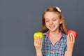 A cute little girl chooses between a green and red Apple on a gray background. The concept of choosing or making a difficult Royalty Free Stock Photo