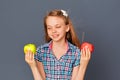 A cute little girl chooses between a green and red Apple on a gray background. The concept of choosing or making a difficult Royalty Free Stock Photo