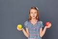 A cute little girl chooses between a green and red Apple on a gray background. The concept of choosing or making a difficult Royalty Free Stock Photo