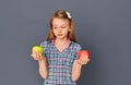 A cute little girl chooses between a green and red Apple on a gray background. The concept of choosing or making a difficult Royalty Free Stock Photo