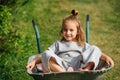 Cute little girl comfortably sitting in a wheelbarrow on a warm summer day Royalty Free Stock Photo