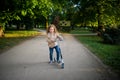 Cute little girl costs with the scooter on a path in city park. Royalty Free Stock Photo