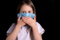 Cute little girl covers her mouth with her hands. The concept of social distancing. On the girl`s face there is a mask to protect Royalty Free Stock Photo