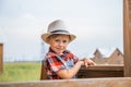 Cute little girl in a cowboy hat standing on a fence of a wooden house Royalty Free Stock Photo