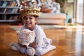 A cute little girl with a crown on her head sitting on the floor at home and posing for a photo while hugging a teddy bear. Family Royalty Free Stock Photo