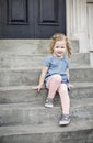 Cute little girl with curly hair sitting on the front steps of her urban home